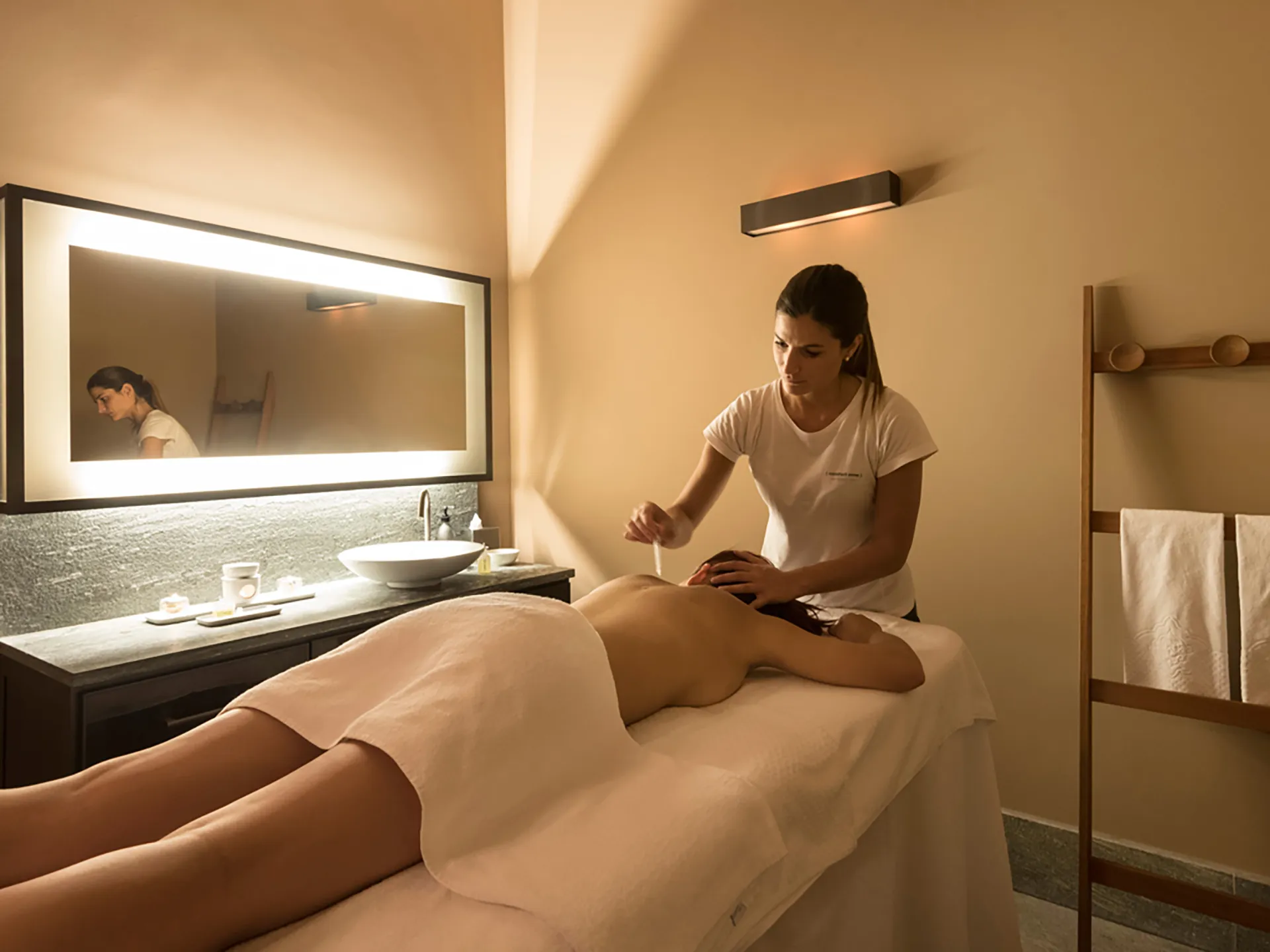 Nell'immagine, la sala massaggi della SPA del Grand Hotel della Posta: si vede una ragazza che sta ricevendo un massaggio stesa a pancia in giù sul lettino. Sulla sinistra, uno specchio rettangolare appeso alla parete e un mobile con un lavabo.