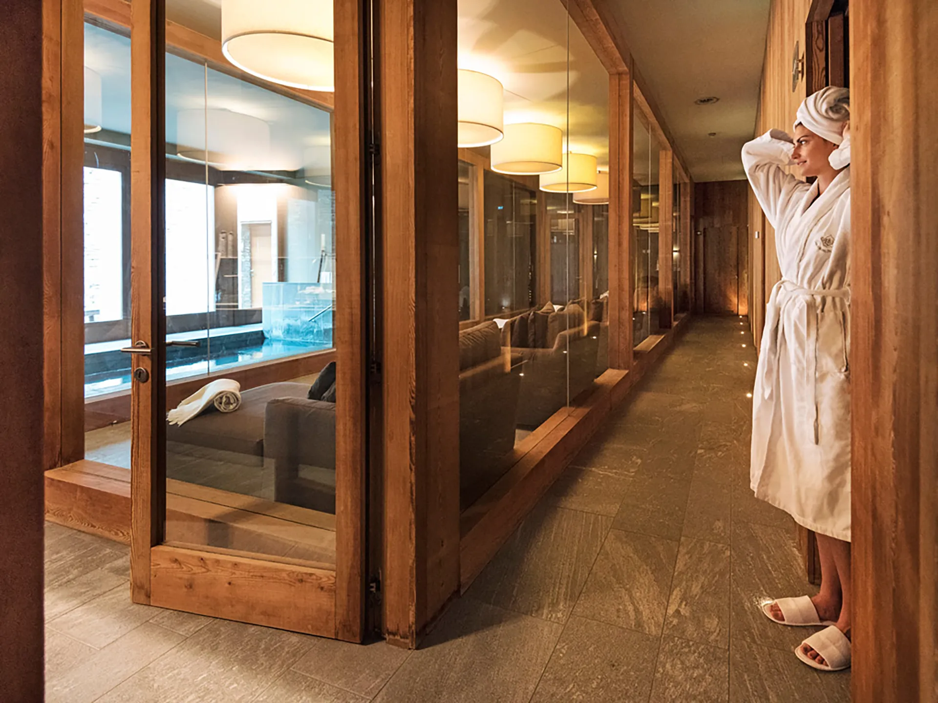 Nell'immagine, l'area relax della SPA del Grand Hotel della Posta: sulla sinistra si vede una ragazza in piedi in accappatoio e ciabattine, con i capelli avvolti in un asciugamano. Di fronte a lei, oltre una porta a vetri, una fila di divanetti e la vasca idromassaggio.