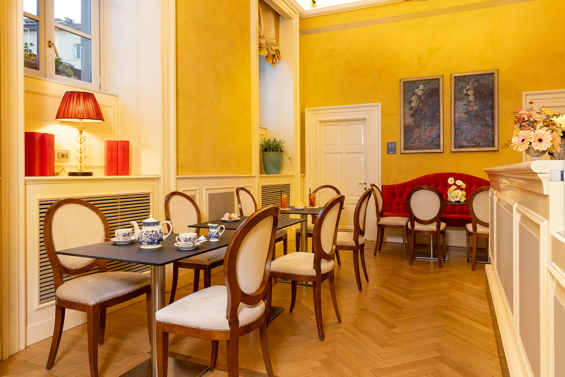 In the picture, the bar of the Grand Hotel della Posta: we can see a few tables and, on the right, the bar counter. On the table in the foreground, there is a teapot with two cups and a milk jug.